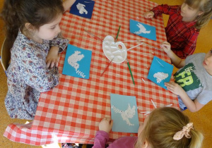 Dzieci wyklejają białym papierem szablon gołąbka.